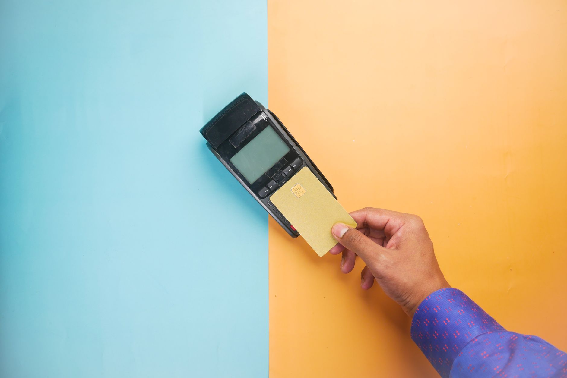 A hand tapping a credit card on a payment terminal for a contactless transaction